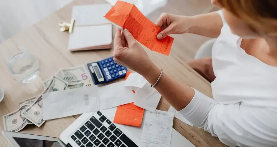 Woman using calculator and receipts at home office desk for finance management.