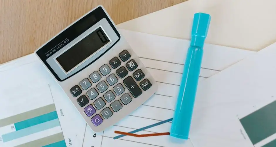 Top view of a calculator and charts on a wooden office desk with a blue marker.