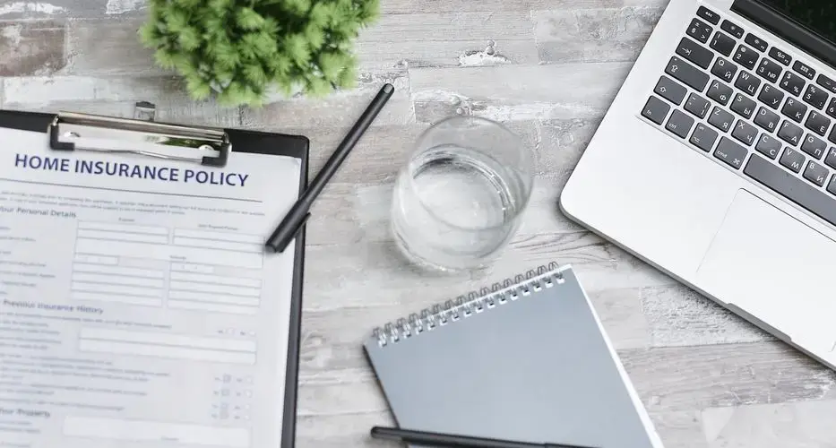 Flat lay of a workspace with a home insurance policy, laptop, and notebook on a desk.
