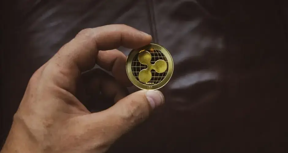 A close-up of a hand holding a gold Ripple cryptocurrency coin, symbolizing digital currency concept.