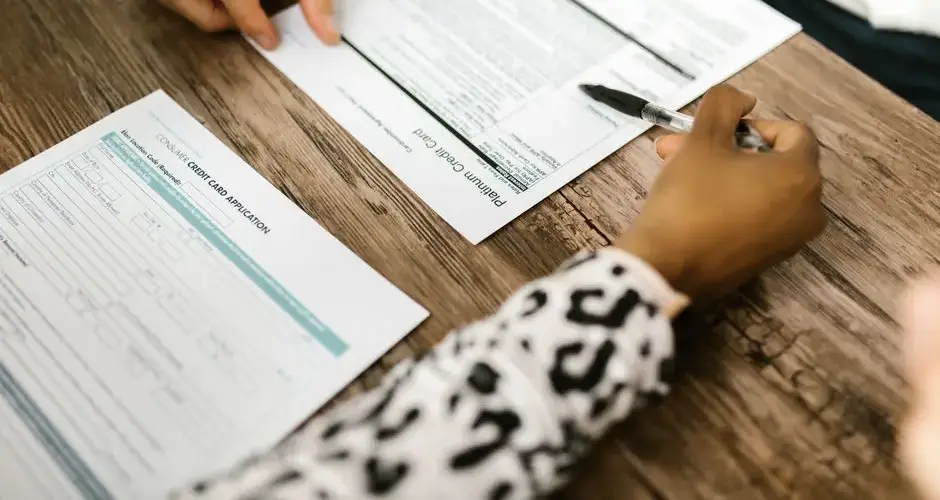 Close-up of two people reviewing and filling out a credit card application on a wooden table.