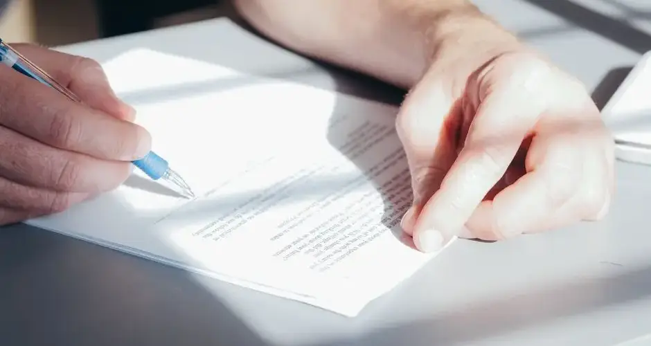Hands signing a contract with a blue pen, close-up view.