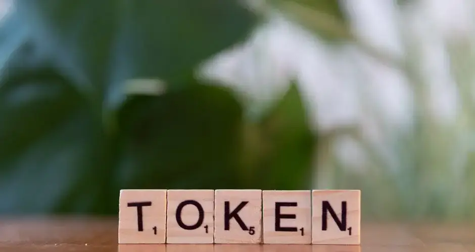 Close-up of Scrabble tiles spelling 'Token' on a wooden surface with a blurred green background.