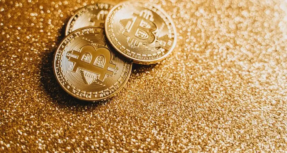 Closeup of three Bitcoin coins on a shimmering gold glitter background, symbolizing digital wealth.
