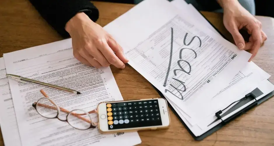 Hands of a person examining tax forms labeled as scam with calculator and papers.