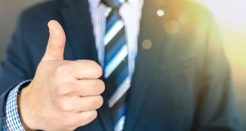 Close-up of a businessman in a suit giving a thumbs-up in a bright, positive setting.