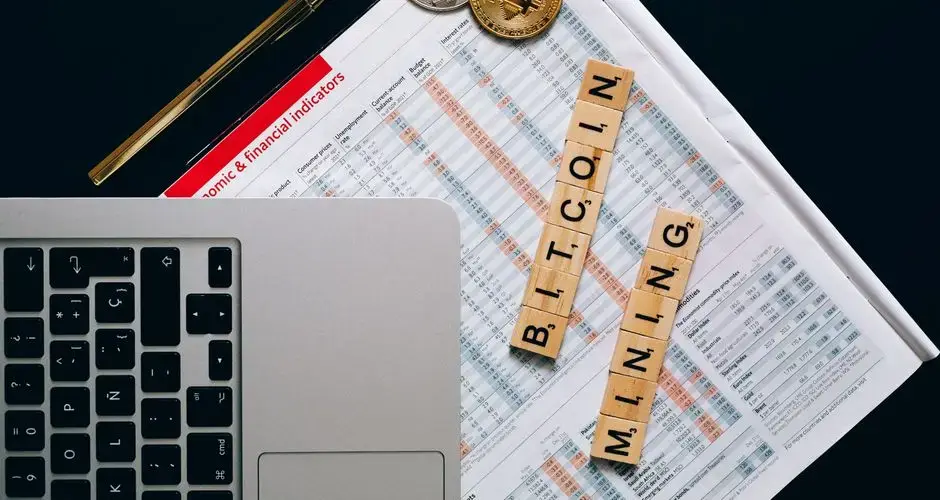 Top view of a laptop, Bitcoin coins, and financial indicators symbolizing Bitcoin mining and investment.