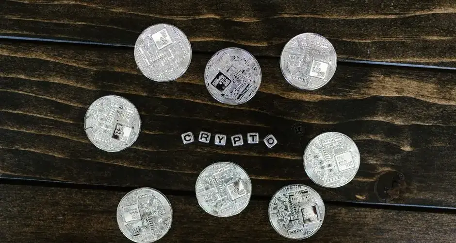 Silver cryptocurrency coins arranged on a wooden surface spelling 'crypto'.