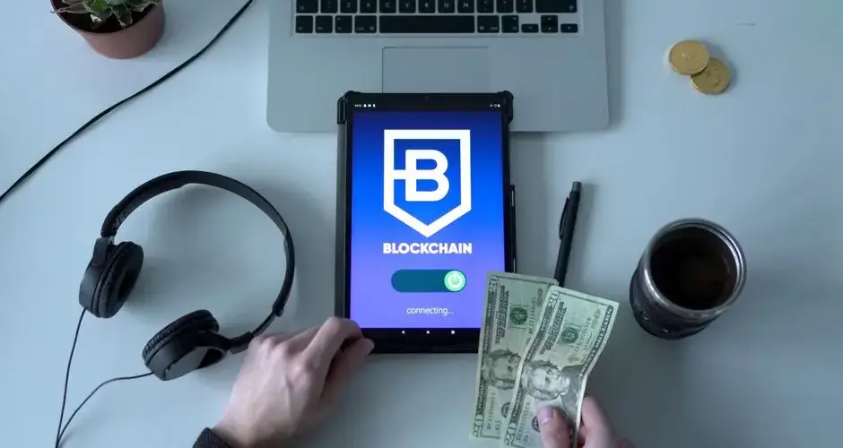 Overhead view of blockchain technology tablet with cash and modern workspace essentials.