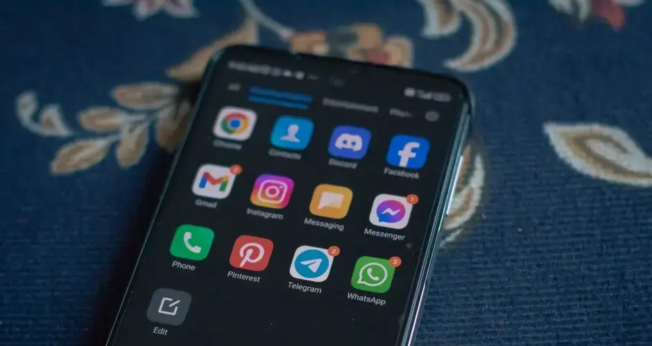 Close-up of a smartphone displaying popular social media apps on a floral fabric surface.