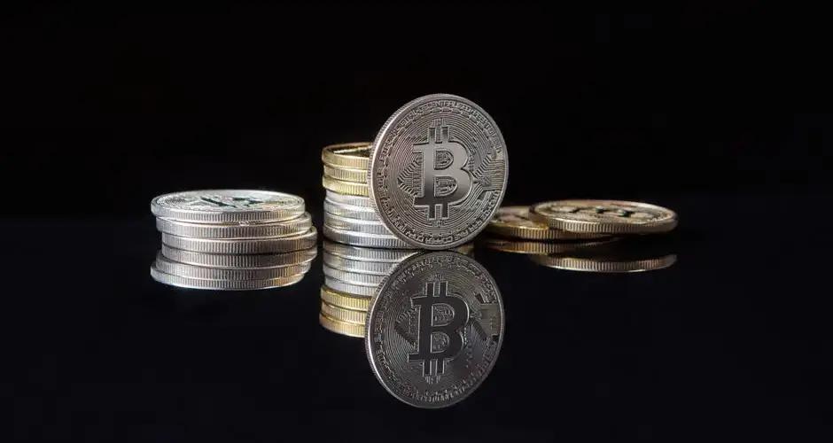 Silver bitcoins stacked on a reflective surface with a dark background, symbolizing cryptocurrency and digital wealth.