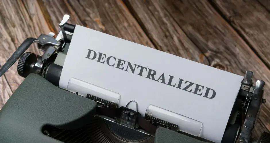 Close-up of a vintage typewriter printing 'DECENTRALIZED' on paper over wooden surface.