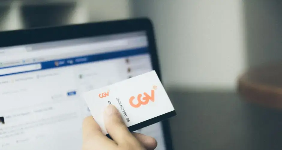 Close-up of a hand holding a card near an active laptop screen, indoors.