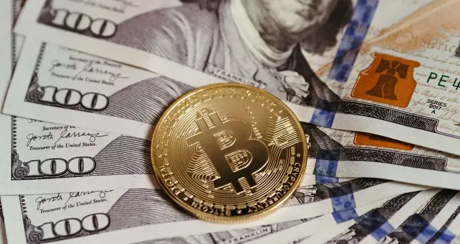 Gold Bitcoin coin resting on US dollar bills showcasing digital and traditional currency.