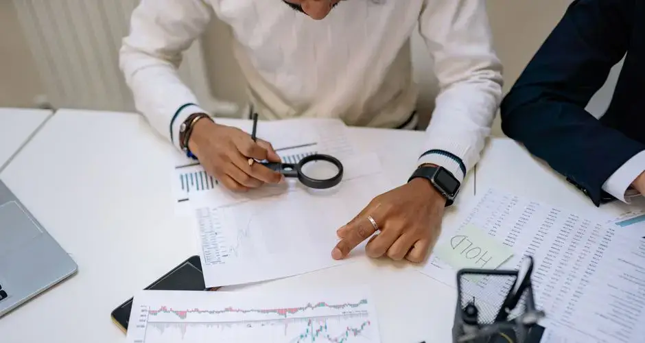Business professionals reviewing charts with a magnifying glass in an office setting.