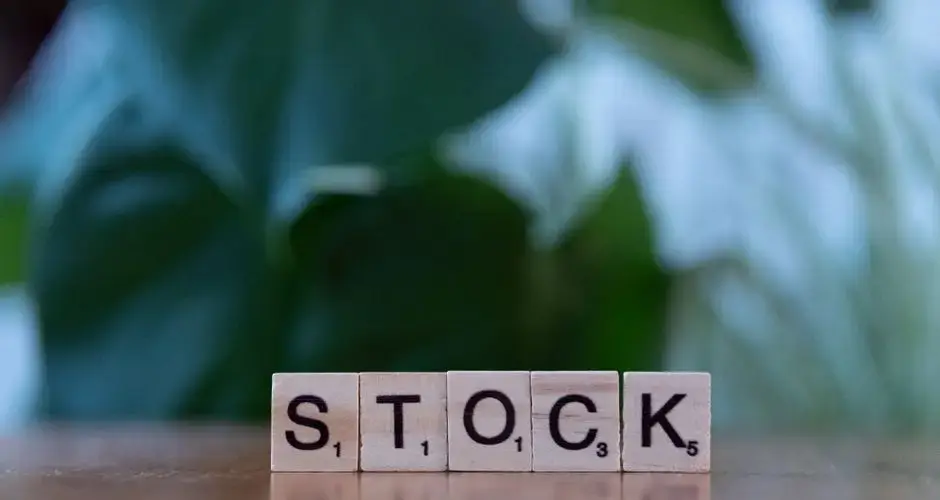 Close-up of wooden letter blocks spelling 'STOCK' on a table against a blurred green background.