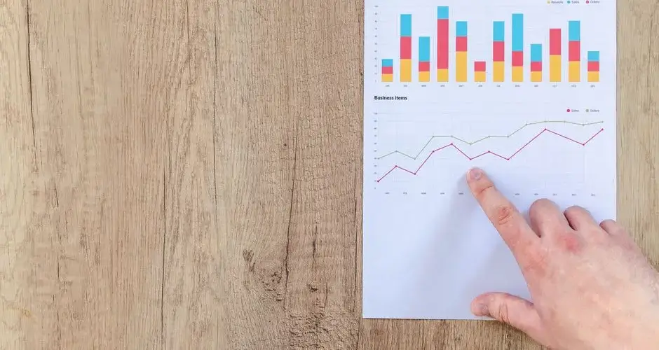 Hand analyzing business graphs on a wooden desk, focusing on data results and growth analysis.