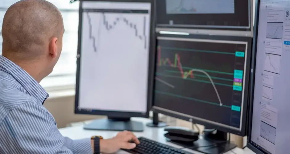 Trader analyzing financial data on multiple monitors in an office setting.