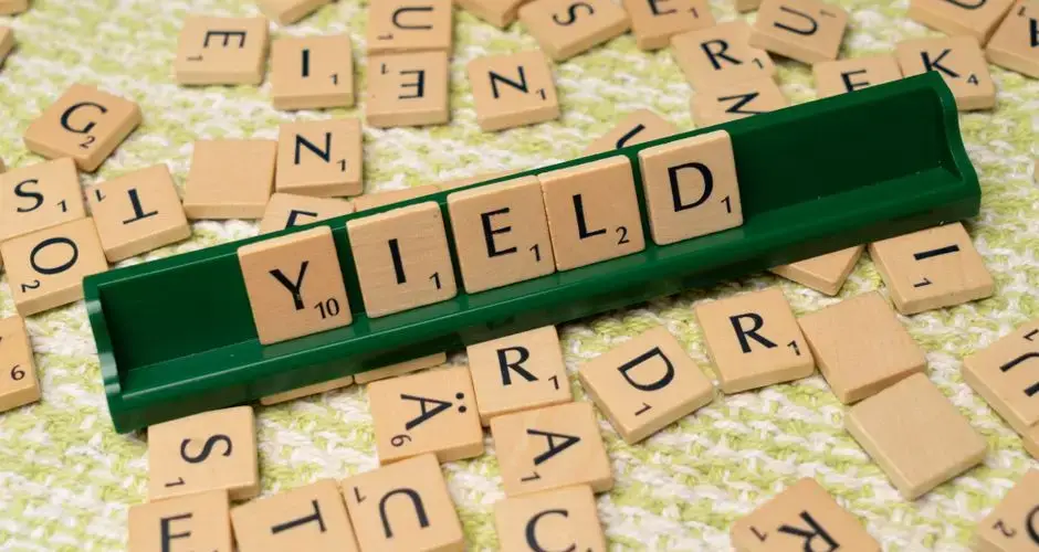 Scrabble tiles spelling 'Yield' on a rack among scattered letters.