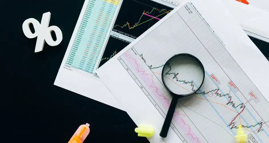 High-angle view of financial charts, showcasing stock market analysis with magnifying glass and highlighters.
