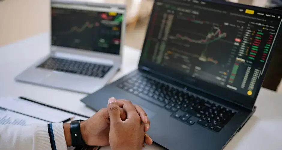 Man seated at a desk using laptops to monitor stock market trends and investments.