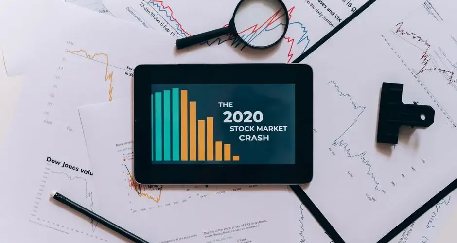 Flat lay of tablet showing 2020 stock market crash with charts and papers.