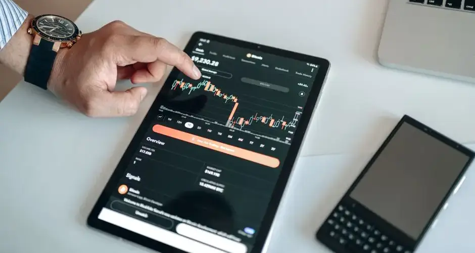 A person using a tablet to view and analyze a cryptocurrency market chart indoors.