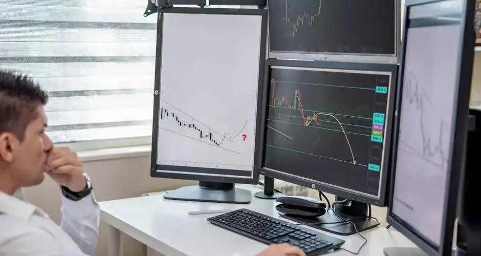 Business professional analyzing financial data on multiple computer monitors at his workspace.