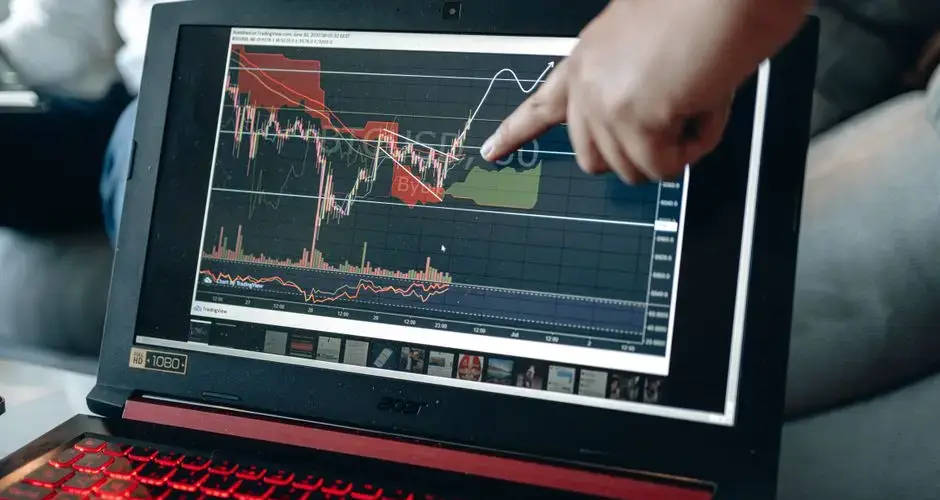 A person points at graph on laptop, analyzing stock trends for investment insights.