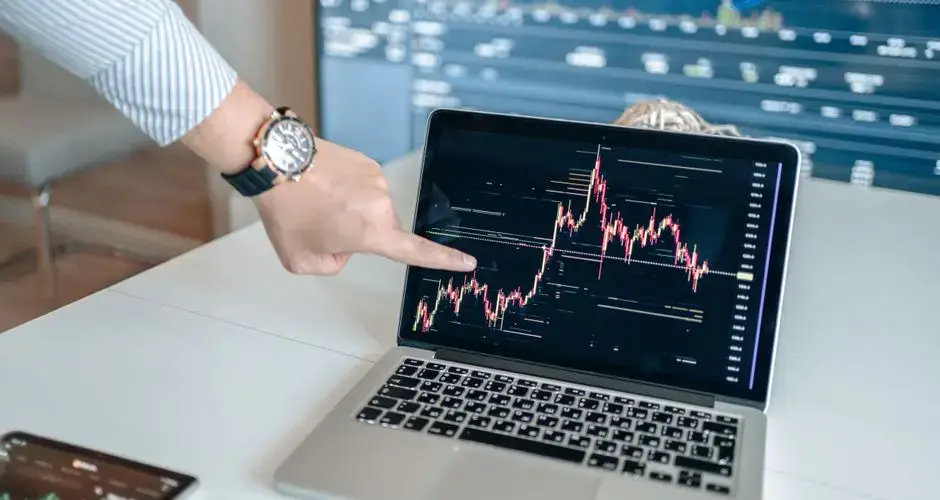 A professional examines financial graphs on a laptop, indicating market trends.