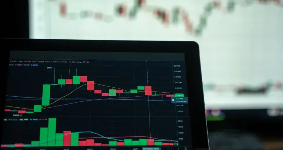 A laptop displays a detailed cryptocurrency trading chart with candlestick patterns.