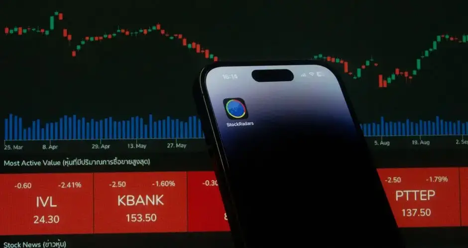 A mobile phone displaying a trading app in front of a financial market chart screen.