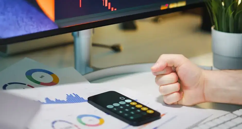Close-up of a desk with financial graphs, a calculator, and a fist symbolizing determination.