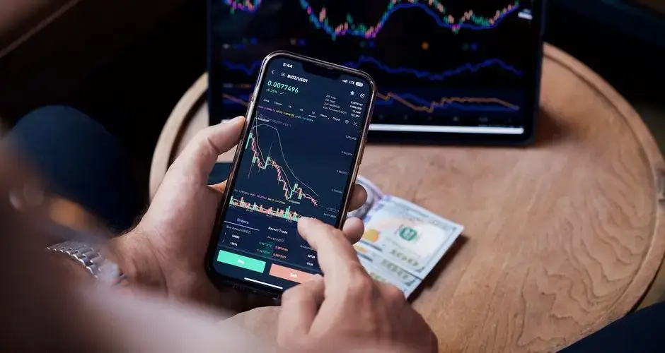 Close-up of a person trading stocks using a smartphone and a tablet.