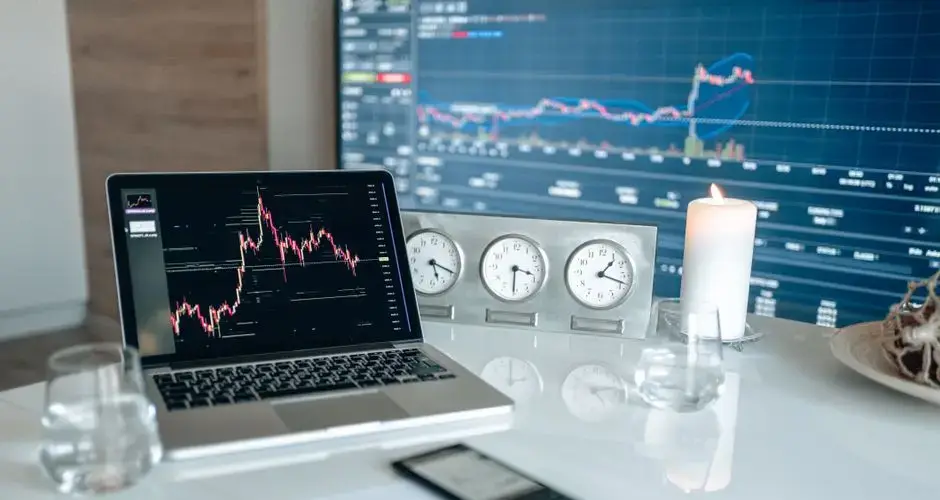 A modern workspace featuring financial charts and multiple clocks on a white table, ideal for trading.