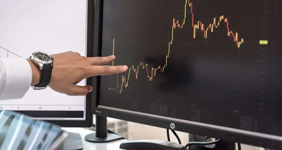 Detailed view of a hand pointing at a cryptocurrency trading graph on a monitor.
