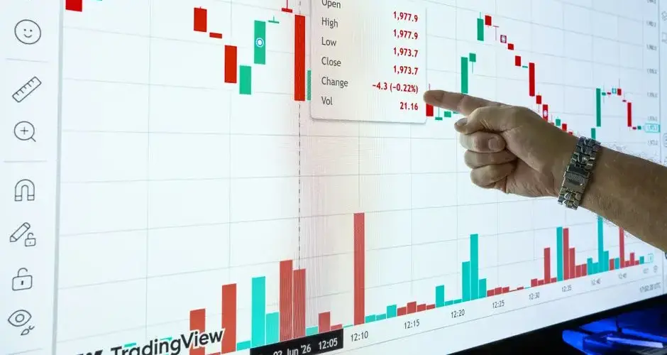 Close-up of a hand pointing at a stock market graph on a screen showing financial data.