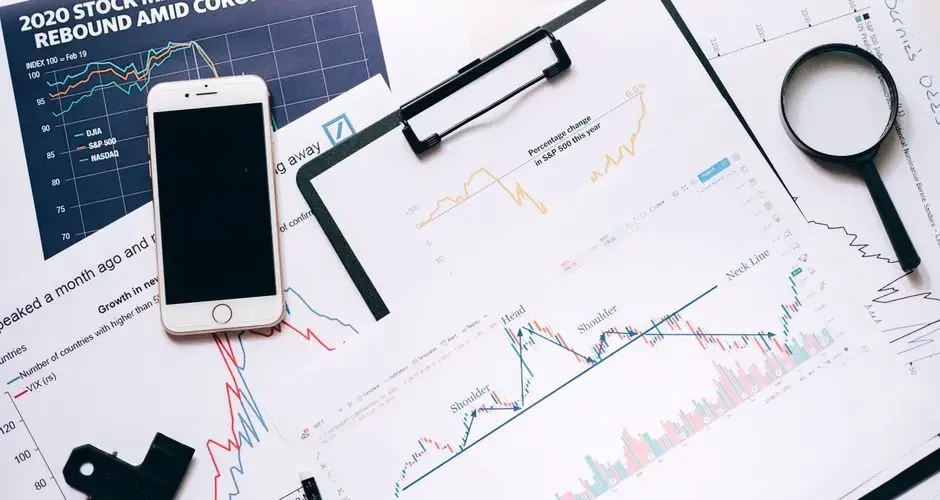 Stock market analysis setup with charts, phone, magnifier, and clipboards.