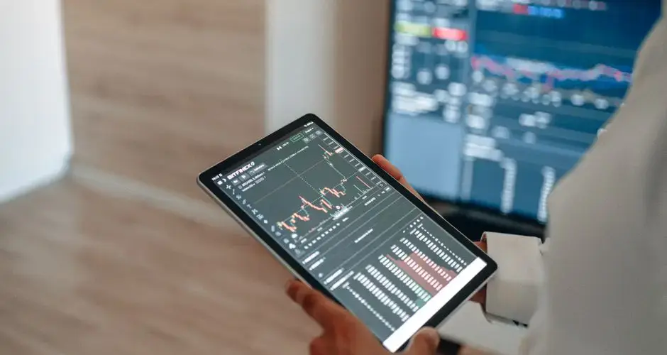 A person uses a tablet to monitor stock market trends and real-time trading graphs.