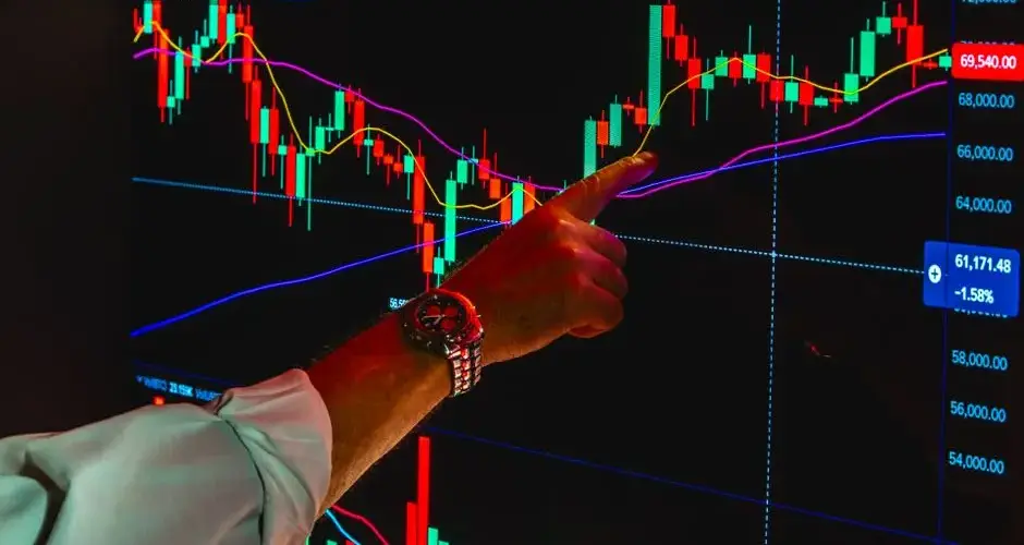 A hand pointing at a crypto market chart displaying Bitcoin trading data and trends.