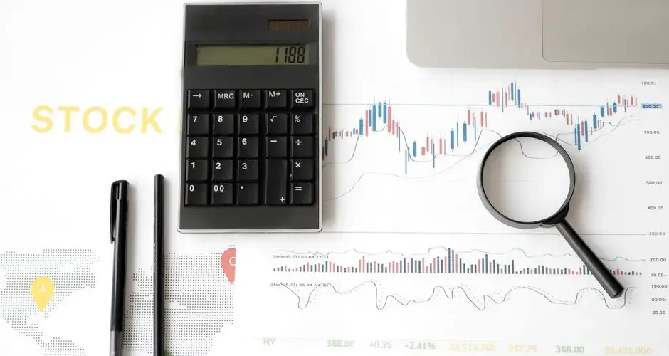 Flat lay of stock market analysis tools including calculator, graphs, and magnifying glass.