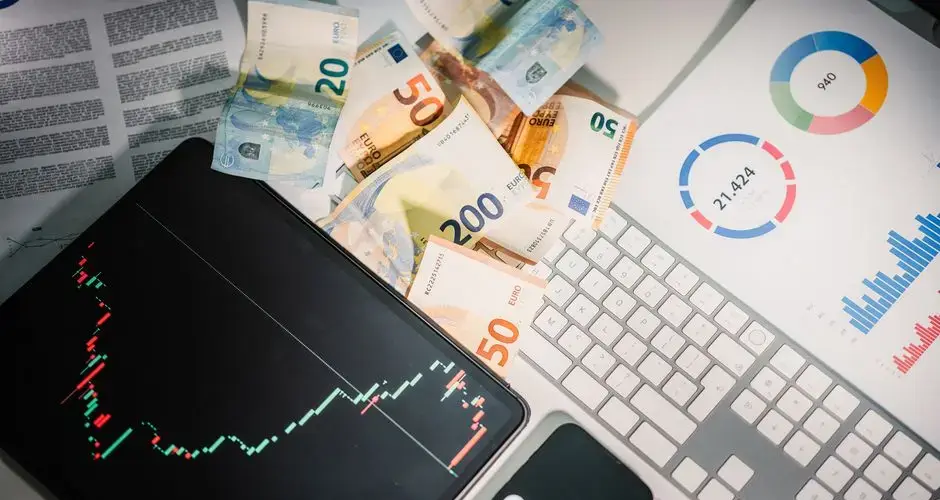 Overhead view of financial tools with Euro banknotes on a desk showing market trends and graphs.