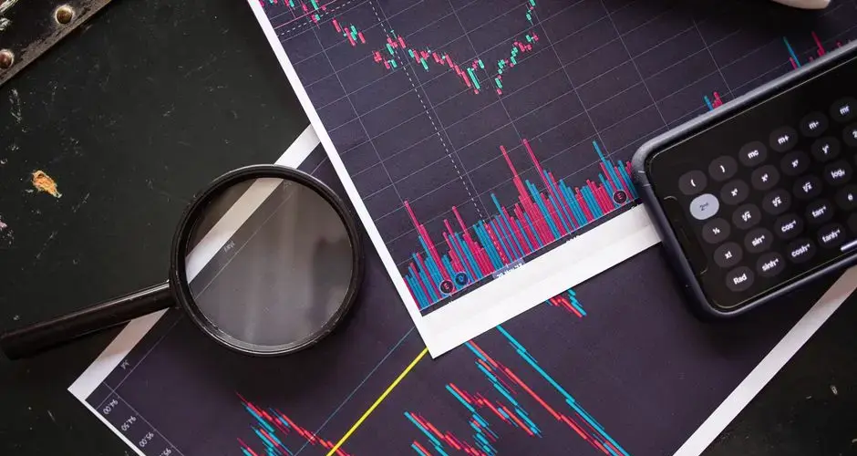 Stock market charts analyzed with a magnifying glass and calculator for financial research.