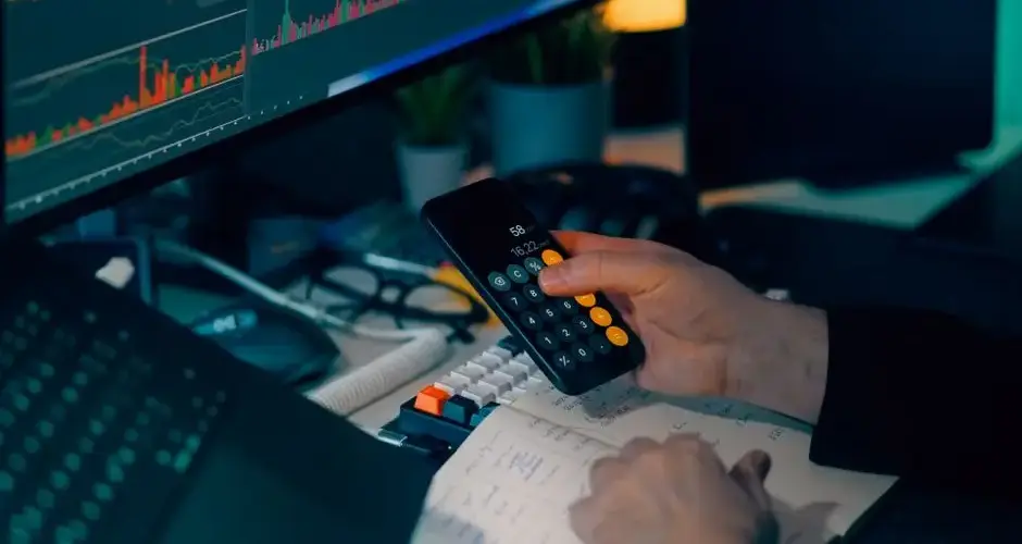 Business analysis with calculator and computer monitor displaying financial graphs and charts.