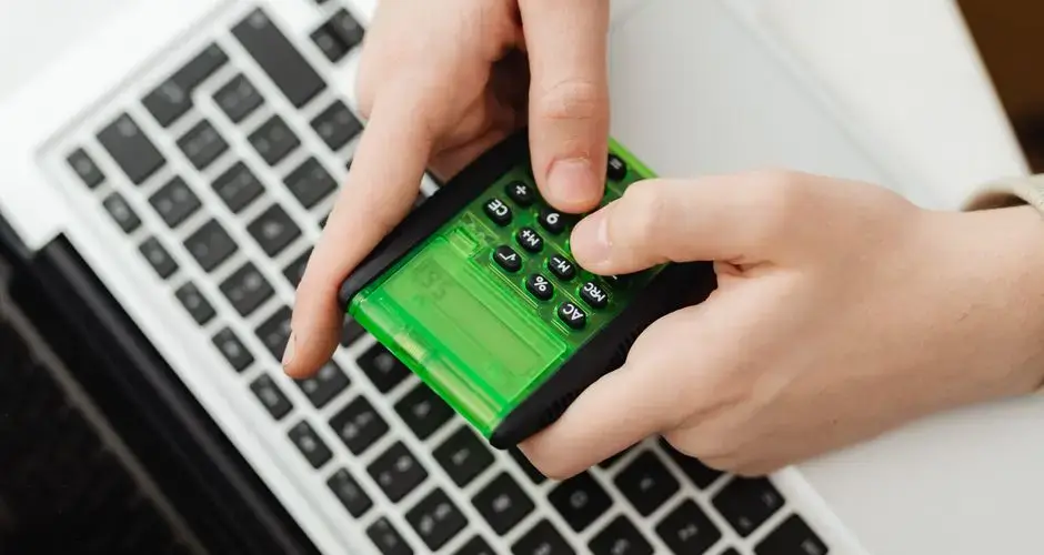 Hands using a green calculator on a laptop keyboard, representing business and finance tasks.