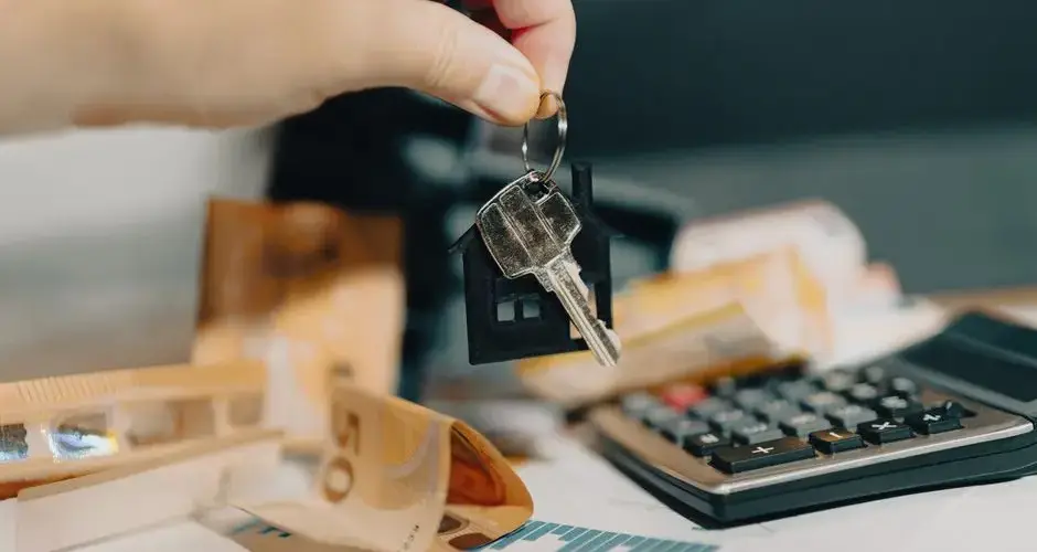 Close-up of a hand holding keys over euros and calculator, symbolizing real estate purchase.