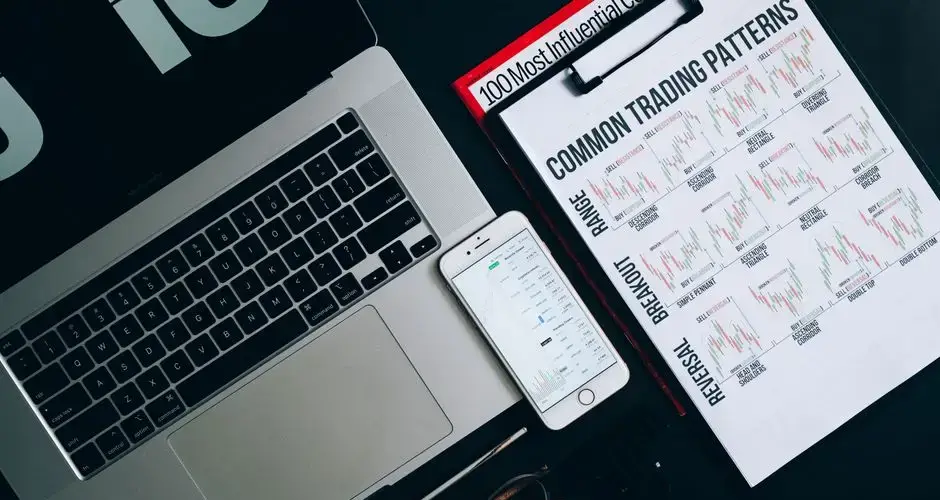 A flat lay composition featuring a laptop, smartphone, and trading pattern charts for financial analysis.