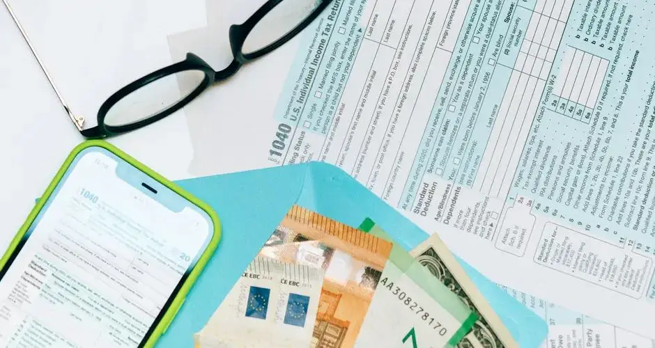 Close-up of tax forms, smartphone, and dollar bills for financial analysis and preparation.