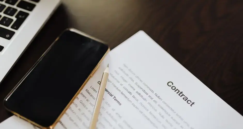 Close-up of a contract document alongside a smartphone and laptop, ideal for business concepts.