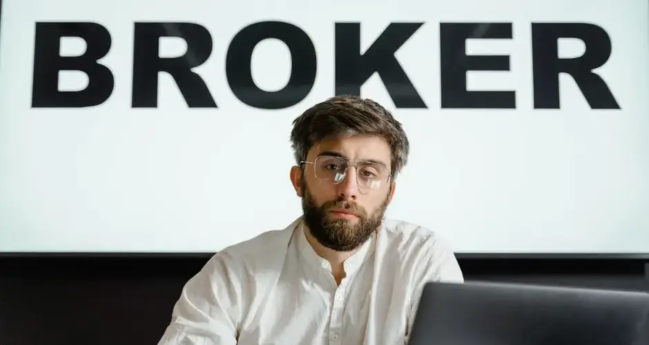 Portrait of a confident businessman sitting in an office under the sign 'BROKER'.